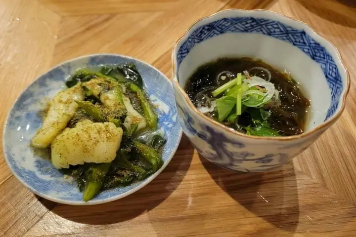 ある居酒屋では、おばんざい３種類から好みのお通しが選べました。写真はイカの山椒和え（左）、もずく酢（右）