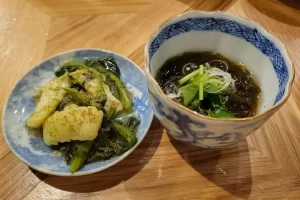 ある居酒屋では、おばんざい３種類から好みのお通しが選べました。写真はイカの山椒和え（左）、もずく酢（右）