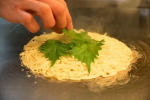 ちんちくりん焼き　調理工程2　鉄板で焼かれるパリパリ生麺の上に青じそをトッピング