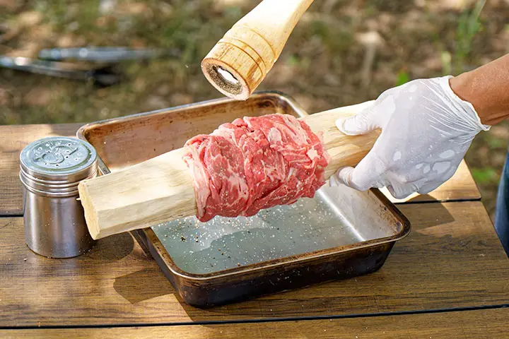 薪に牛肉を巻き付けながら塩、コショウをふる